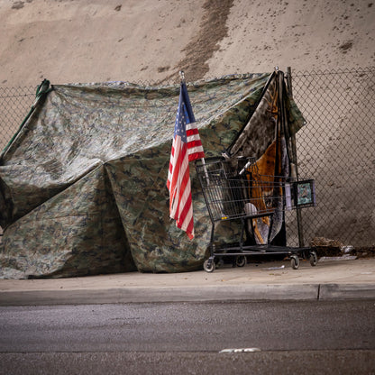 Camouflage tent with American flag and shopping cart on a street corner