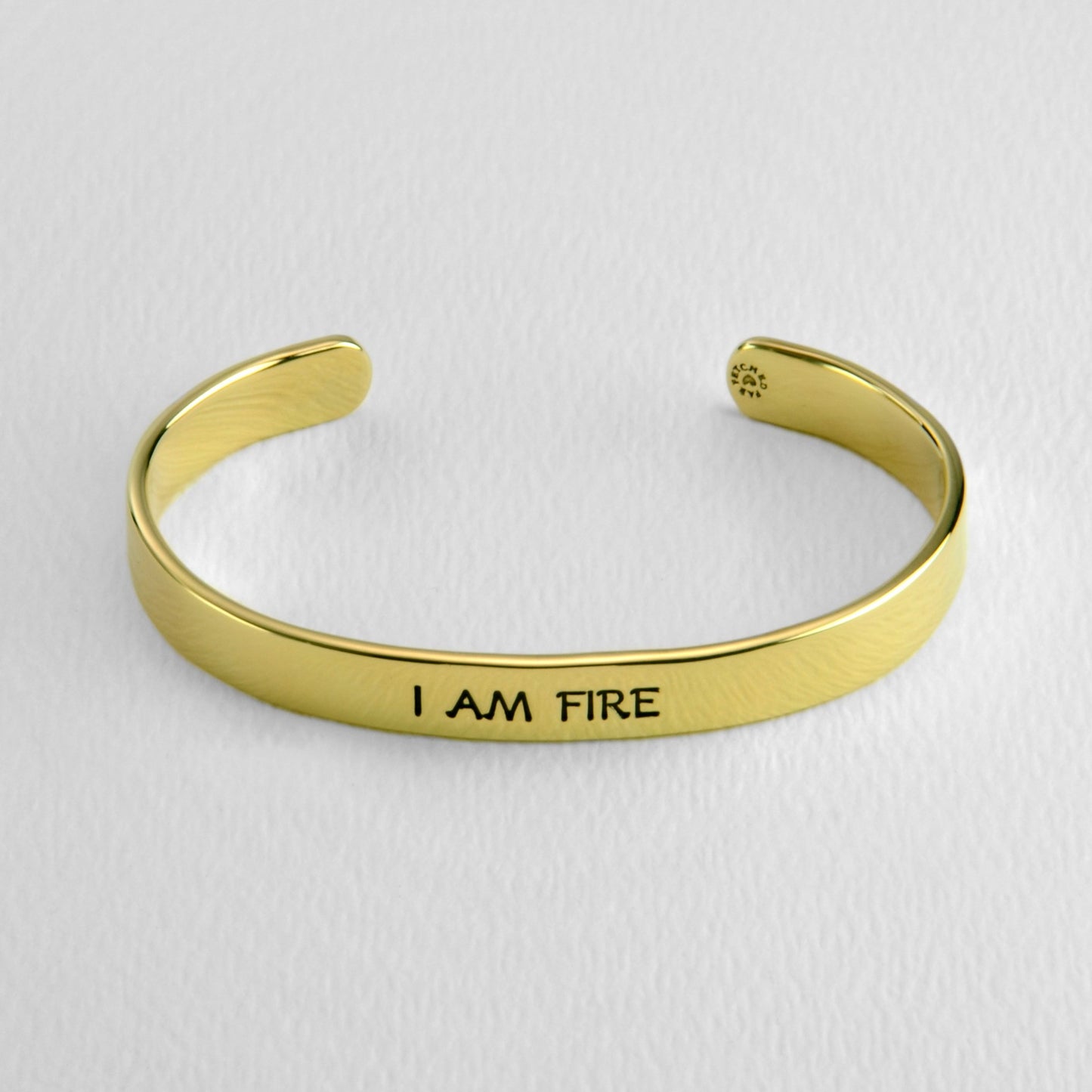 Brass bracelet with 'I AM FIRE' engraving on a light gray background