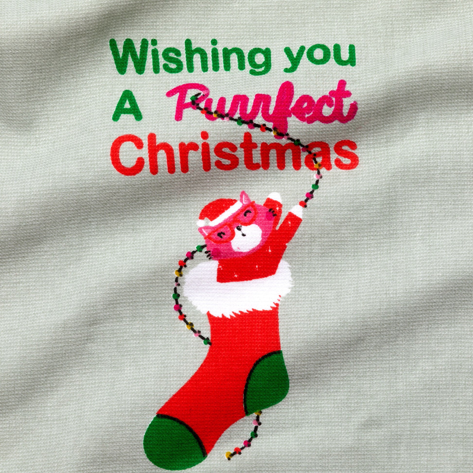 Printed design of a cat in a red stocking with text 'Wishing you a purrfect Christmas' on a fabric background.

