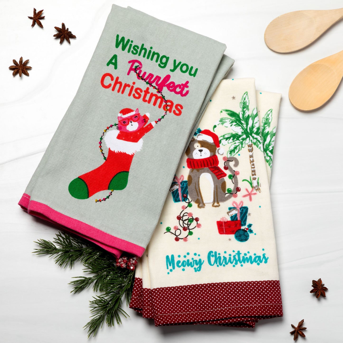 Two Christmas-themed kitchen towels on a white surface with decorative items.