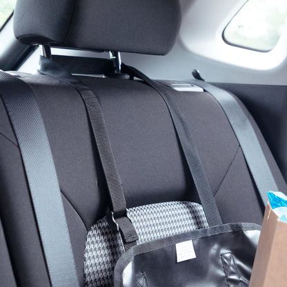 A black car seat belt organizer hanging from a car seat, holding a black bag and a patterned item, shown inside a vehicle.