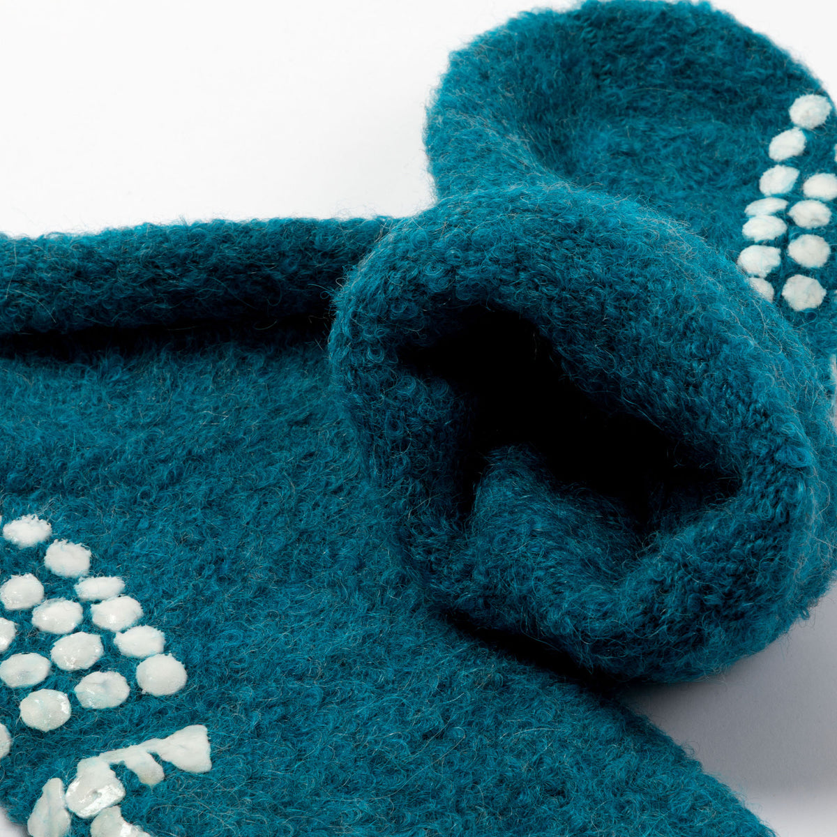 A close-up of a teal blue fuzzy knit textile slipper sock featuring white textured accents on a white background.
