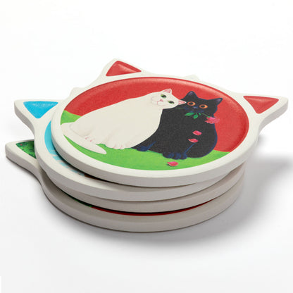 A stack of round cat-shaped coasters with ears, featuring a colorful illustration of a white cat and a black cat on a red and green background.