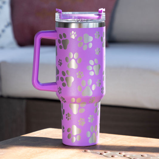 A purple Paw Print Vacuum Sealed Stainless Steel Tumbler - 40 oz sitting on a table outside.