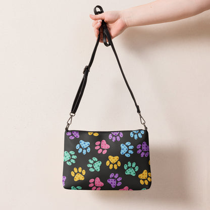 Handbag with colorful paw prints held by a hand against a beige background