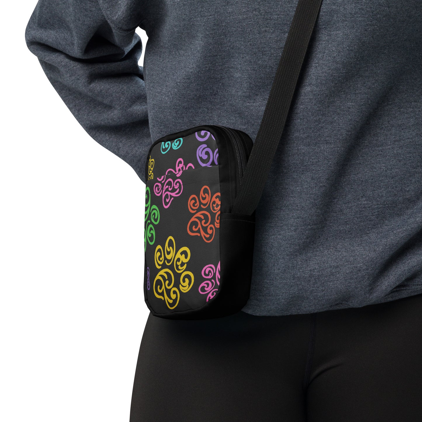 Person wearing a black crossbody bag with colorful patterns on a white background