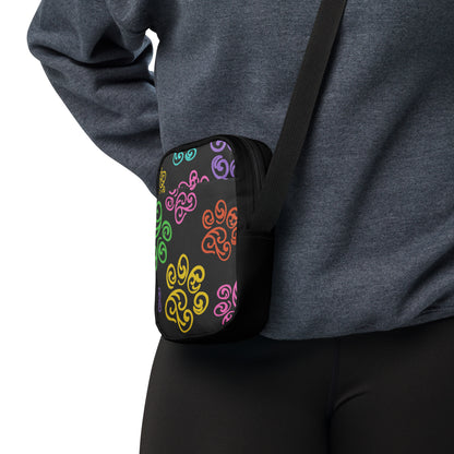 Person wearing a black crossbody bag with colorful patterns on a white background
