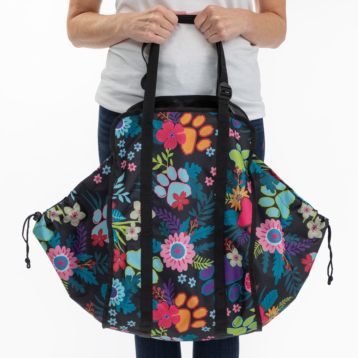 A person holding a large black duffel bag with a colorful floral and paw-print pattern, shown against a plain white background.