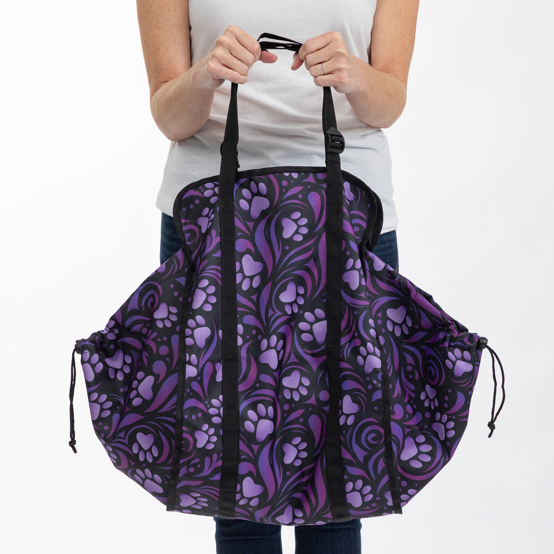 A person holding a large tote bag with a purple and black paw-print pattern, shown against a plain white background.