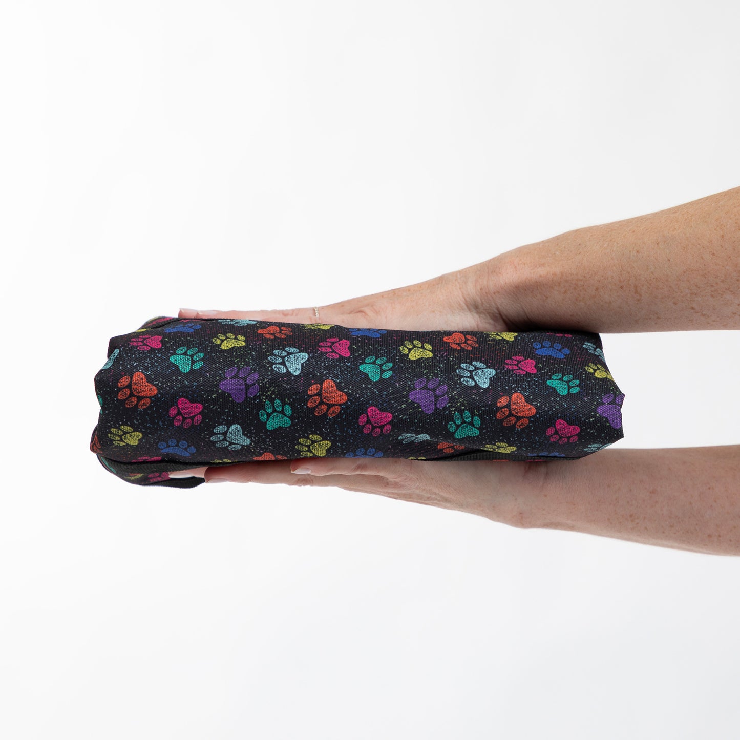 A person's hands holding a black zippered pouch or small bag covered in a colorful paw print pattern against a plain white background.