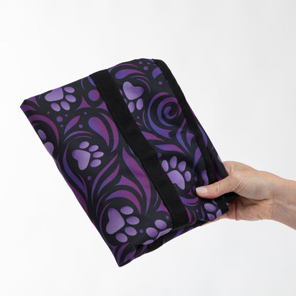 A hand holding a small zippered pouch or bag with a black and purple paw-print pattern, shown against a plain white background.