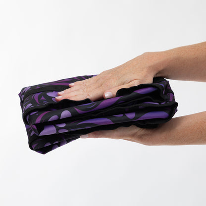 A person's hands holding a folded black bag item with a purple abstract flame-like pattern against a plain white background.
