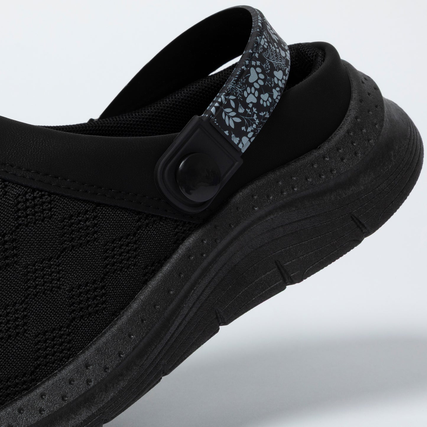 Black clog shoe with a strap on a light gray background
