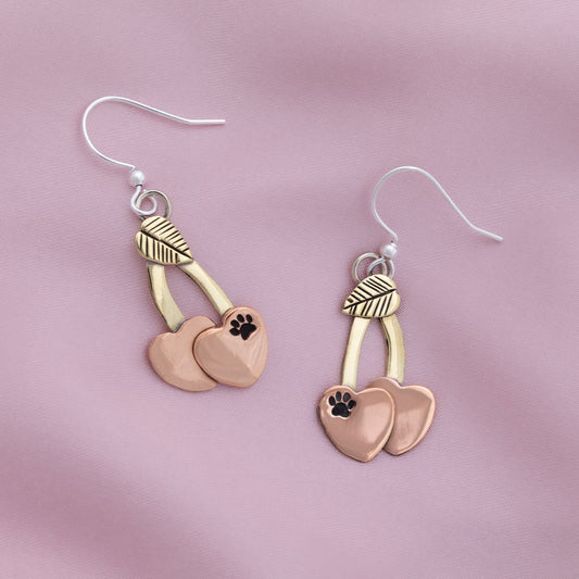 Pair of earrings with heart and paw print design on a pink background