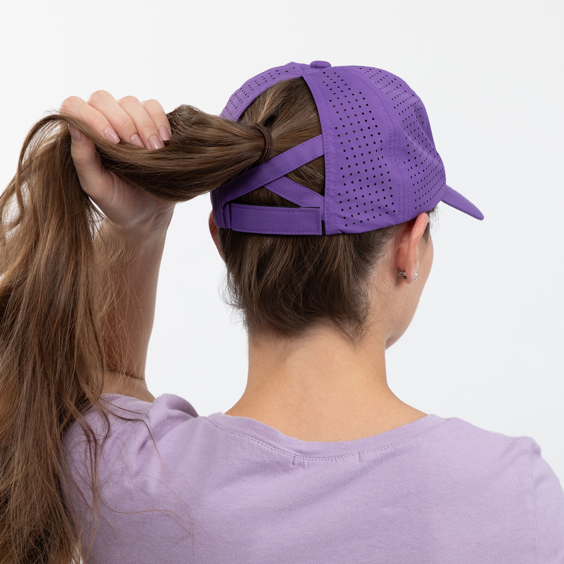 Person wearing a purple cap and shirt, adjusting their hair against a white background