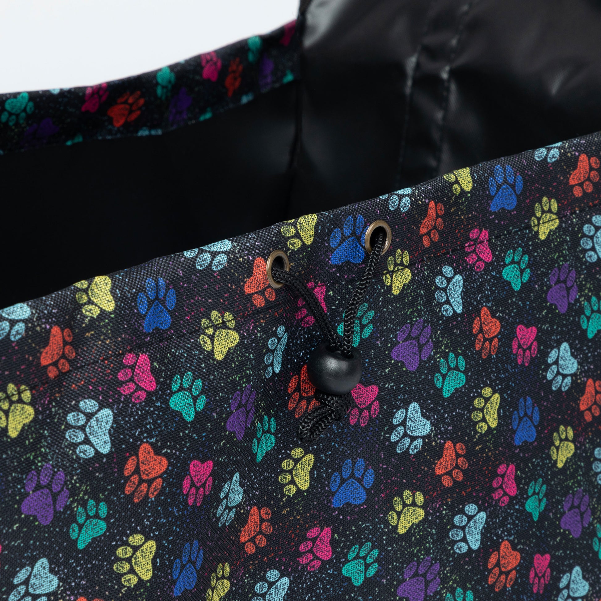 Close-up of a black fabric tote bag with a colorful paw print pattern and a black drawstring closure.