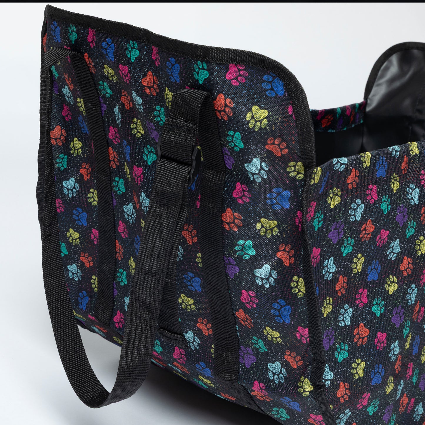A black collapsible organizer bag with a colorful paw print pattern, featuring black webbed handles and a black interior lining, shown on a light gray background.