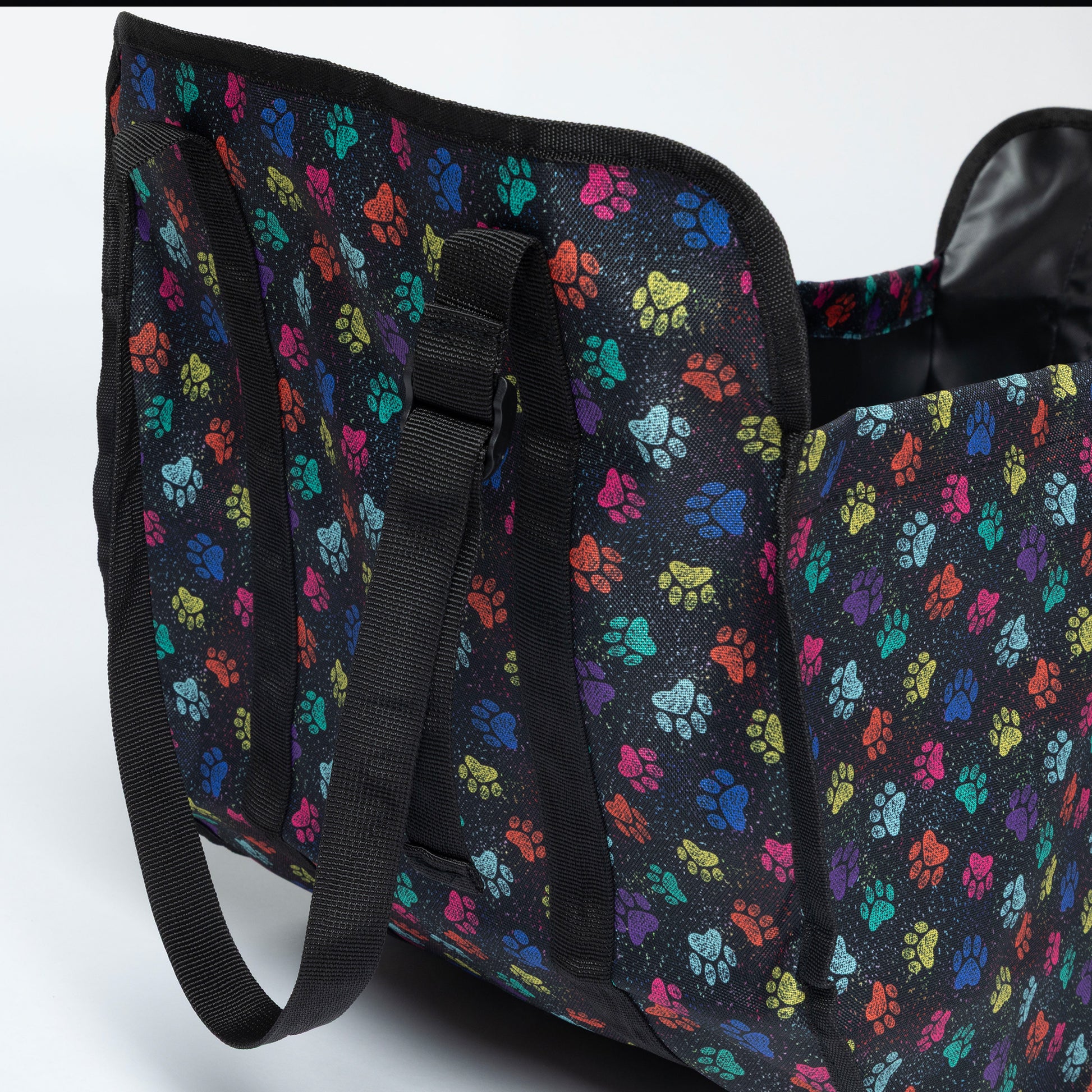 A black collapsible organizer bag with a colorful paw print pattern, featuring black webbed handles and a black interior lining, shown on a light gray background.