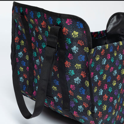 A black collapsible organizer bag with a colorful paw print pattern, featuring black webbed handles and a black interior lining, shown on a light gray background.