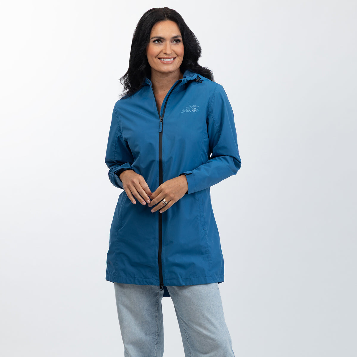 A woman modeling a blue lightweight zip-up jacket with a small white logo on the left chest, paired with light gray jeans, against a plain light gray studio background.