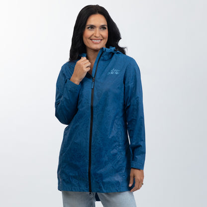 A woman wearing a blue hooded rain jacket with a subtle tonal pattern, standing against a light gray studio background.