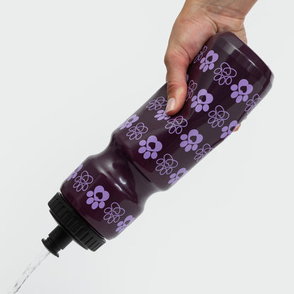 Hand holding a purple water bottle with a floral pattern, water pouring out.