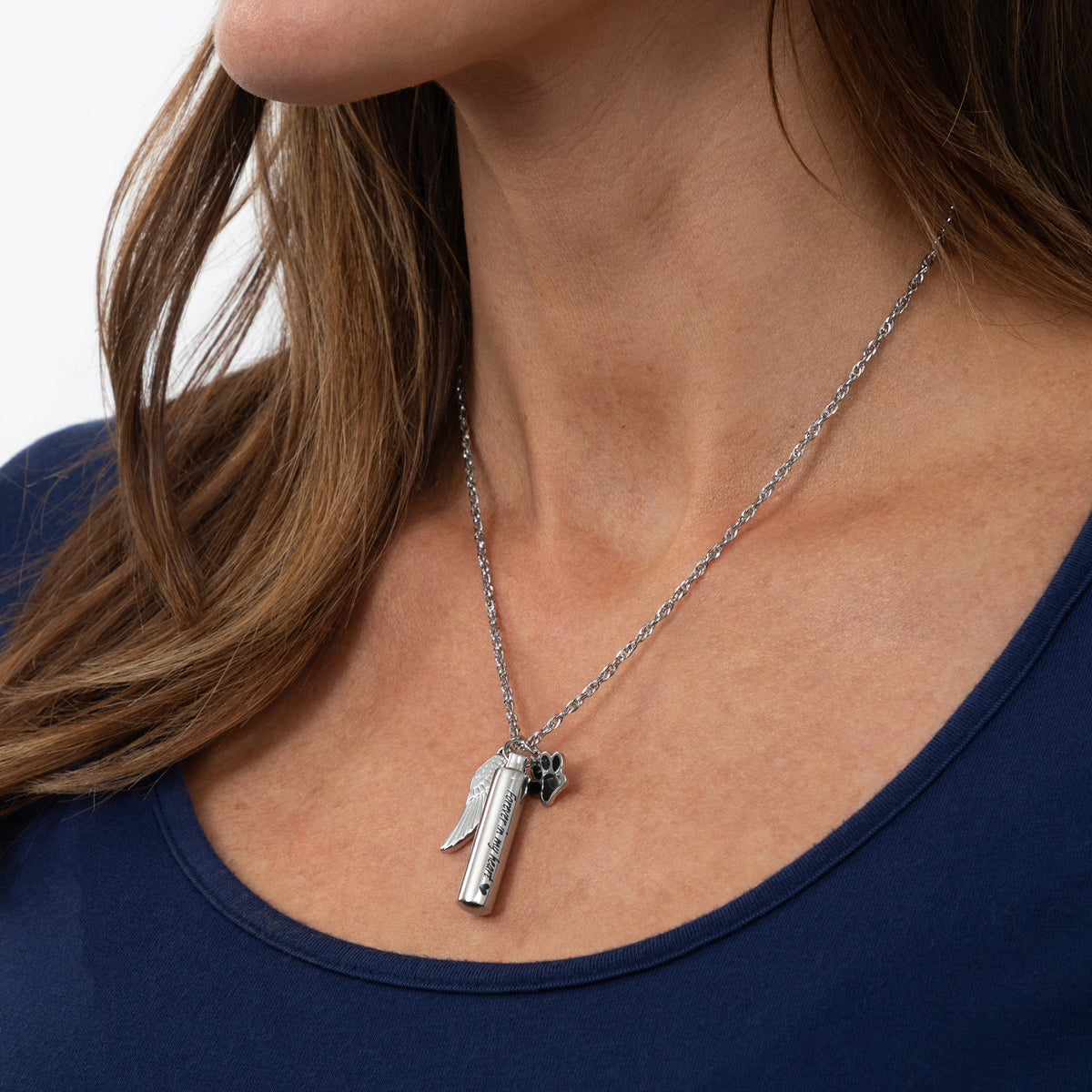 A close-up of a woman wearing a silver pendant necklace with a small angel and cross charm, paired with a navy blue top.