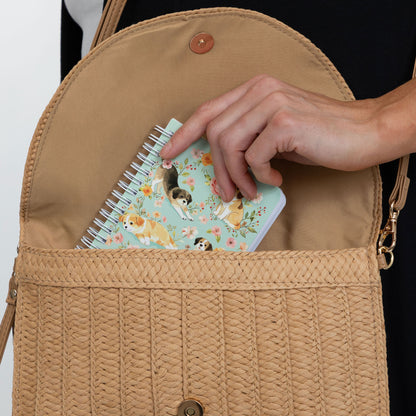 A close-up of a tan woven crossbody bag being opened by a person, with a floral spiral notebook peeking out from the pocket.