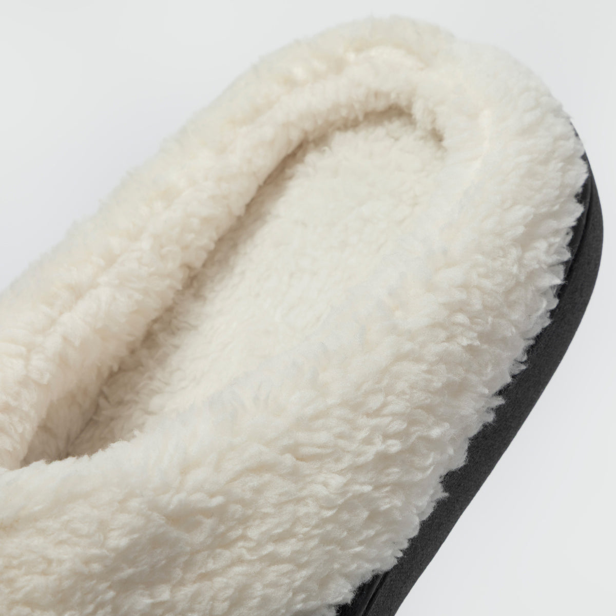 Close-up of a fluffy cream sherpa-lined slipper showing the soft interior lining and a black outer edge on a light gray background.