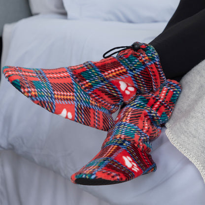 A person wearing red plaid slipper socks with white paw prints, resting on a white bed.