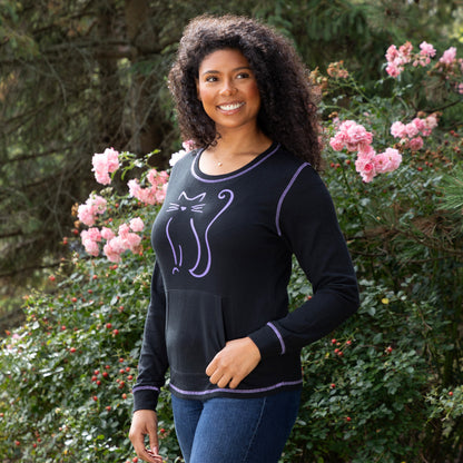 Smiling woman outdoors in a cat-themed black thermal long sleeve top surrounded by colorful flowers.