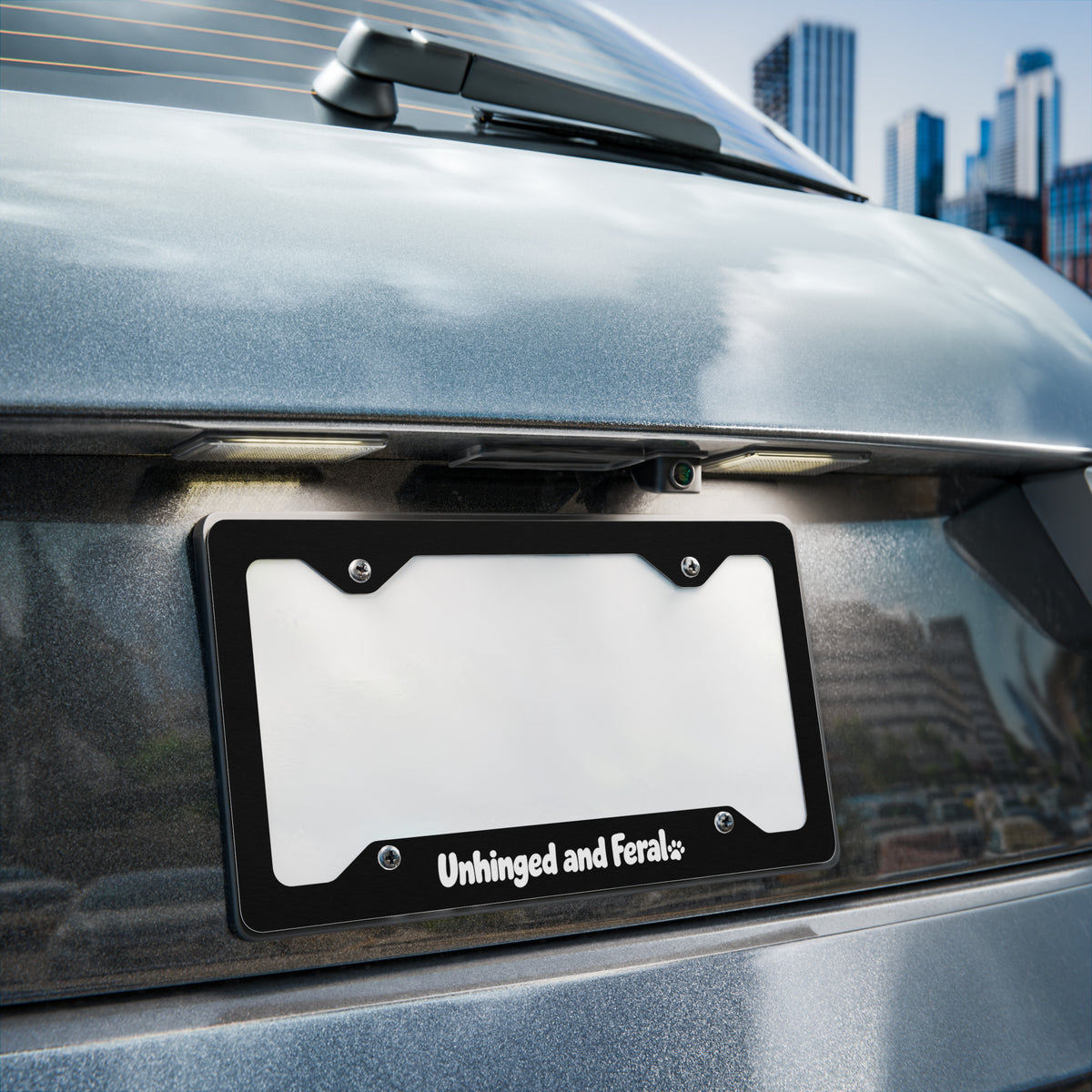 Car license plate frame with 'Unhinged and Feral' on a vehicle in an urban setting.