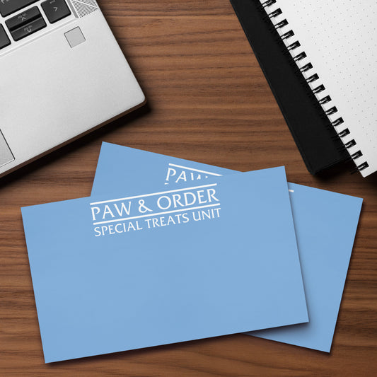 Two sticky note pads with 'Paw & Order Special Treats Unit' text on a wooden surface with a laptop and notebook.