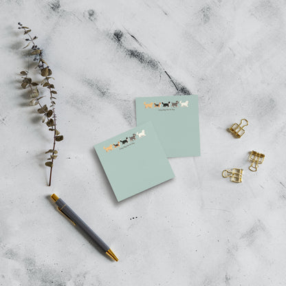 Two 3x3 mint green notepads with a cute dog illustration and the text 'Every Dog has Its Day' at the top, styled on a light gray marble background with a gray pen, gold paperclips, and a dried eucalyptus branch.
