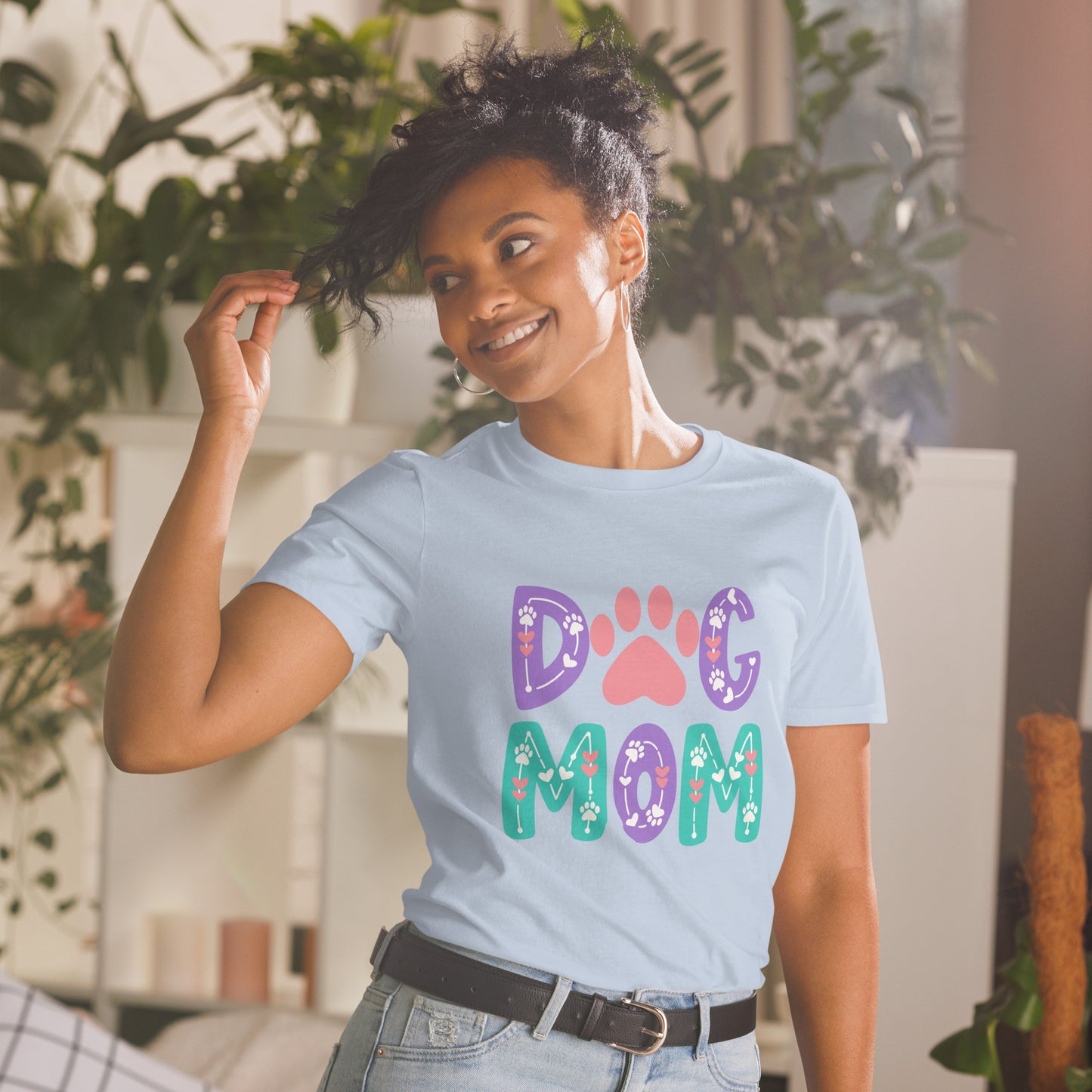 Woman wearing a light blue t-shirt with 'Dog Mom' text and paw prints in a home setting.