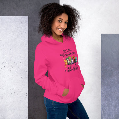 A woman wearing a bright pink hoodie with a graphic that reads 'RELAX We're all crazy it's not A COMPETITION' with cartoon animals, paired with blue jeans, set against a split gray and white textured background.