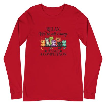 A red long-sleeve crewneck t-shirt with a graphic print of seven colorful cartoon cats sitting on a scale, with the text 'RELAX. We're all crazy IT'S NOT A COMPETITION' in dark lettering.