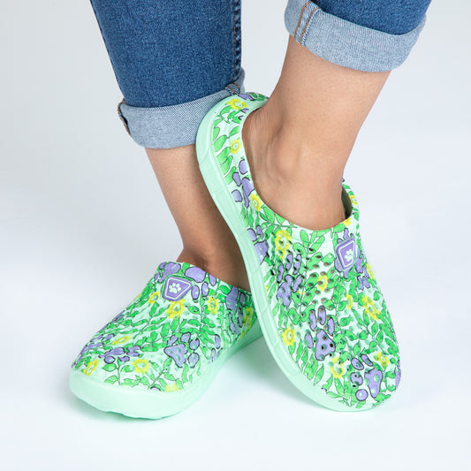 Person wearing colorful floral and paw print clogs paired with rolled-up jeans, showcasing a vibrant style.