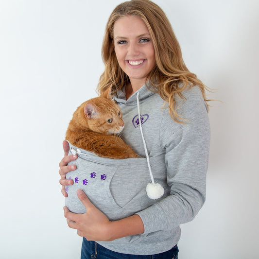 Woman smiling while holding an orange cat in a cozy kangaroo pouch sweatshirt.
